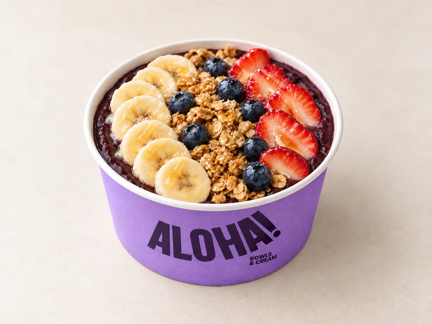 Açaí bowl topped with banana, granola, blueberries and strawberries in an ALOHA! cup